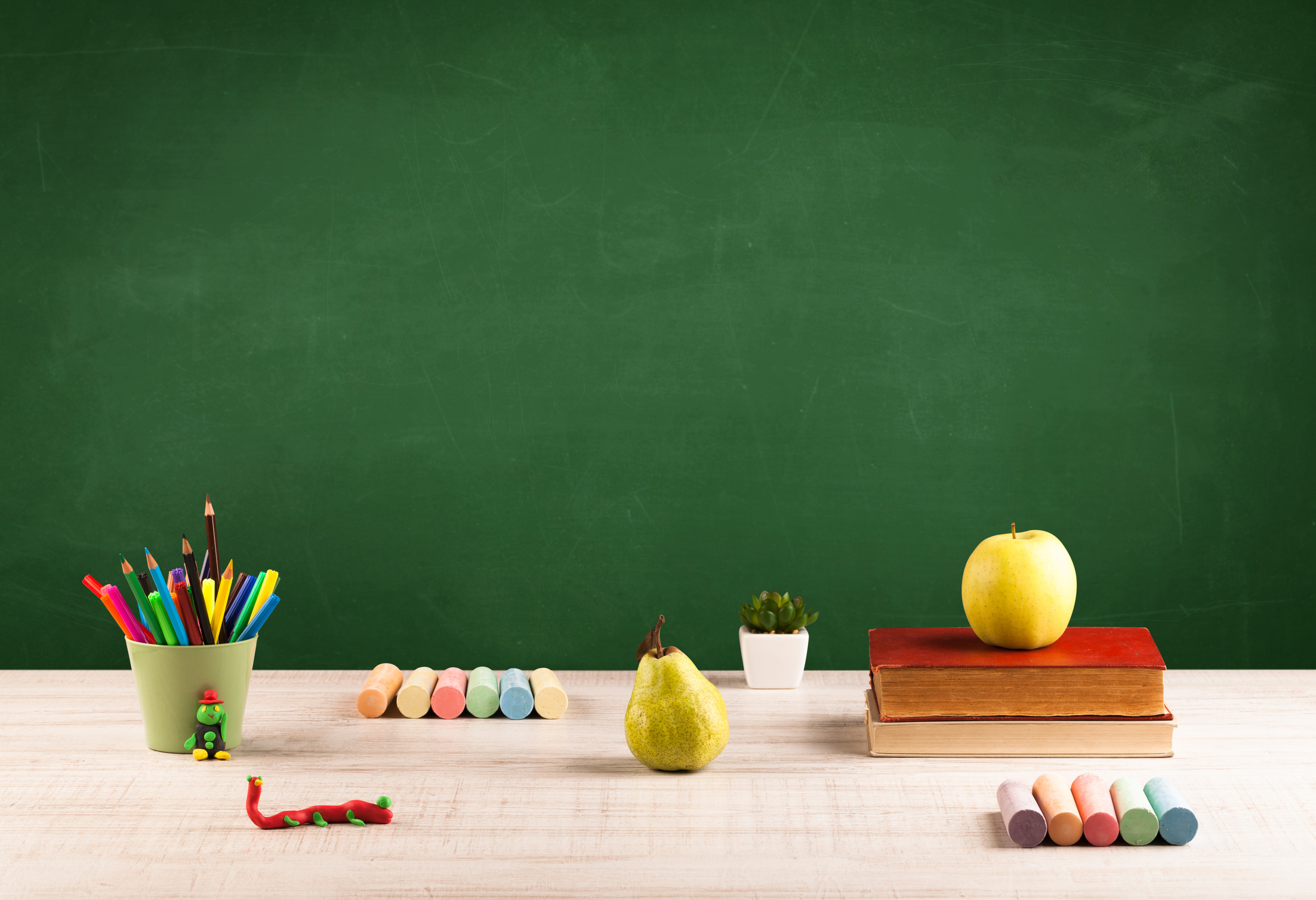 School items on desk with empty chalkboard